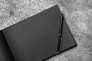 Photo of Open sketchbook with black pages and pen on grey stone table, top view