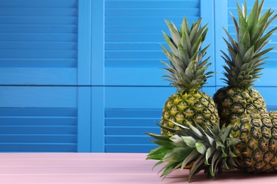 Photo of Delicious ripe pineapples on pink table near blue wall. Space for text