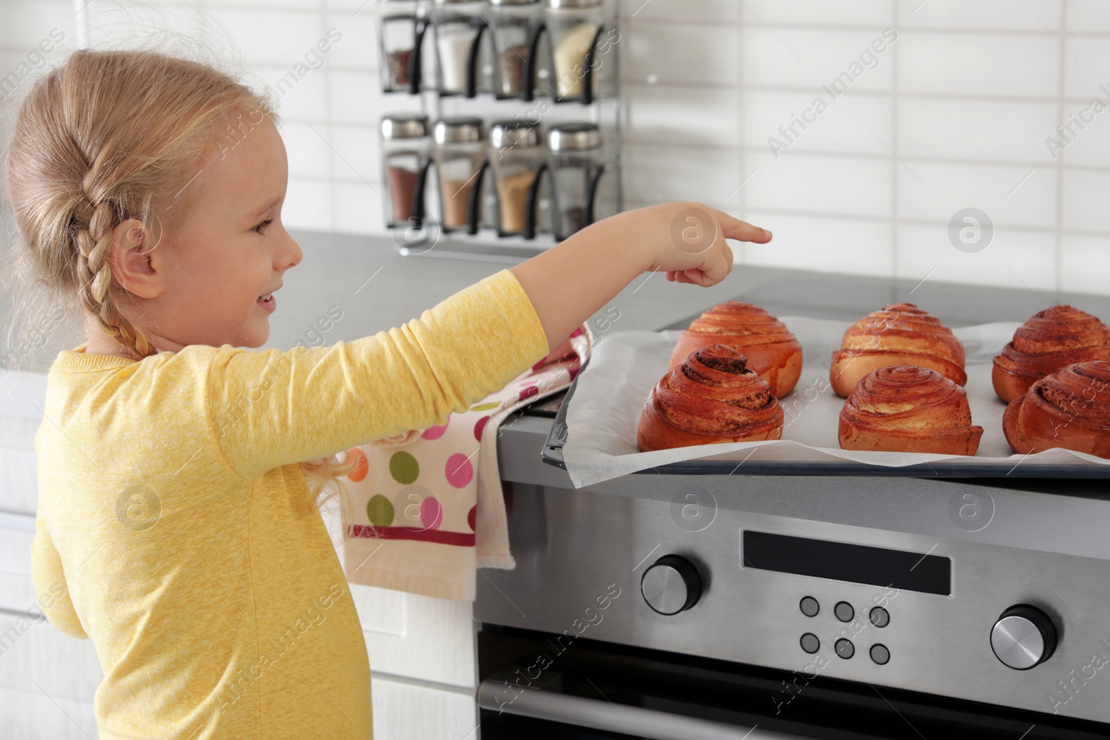 Photo of Little girl with tray of oven baked buns in kitchen