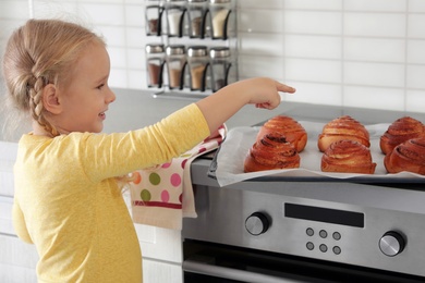 Photo of Little girl with tray of oven baked buns in kitchen