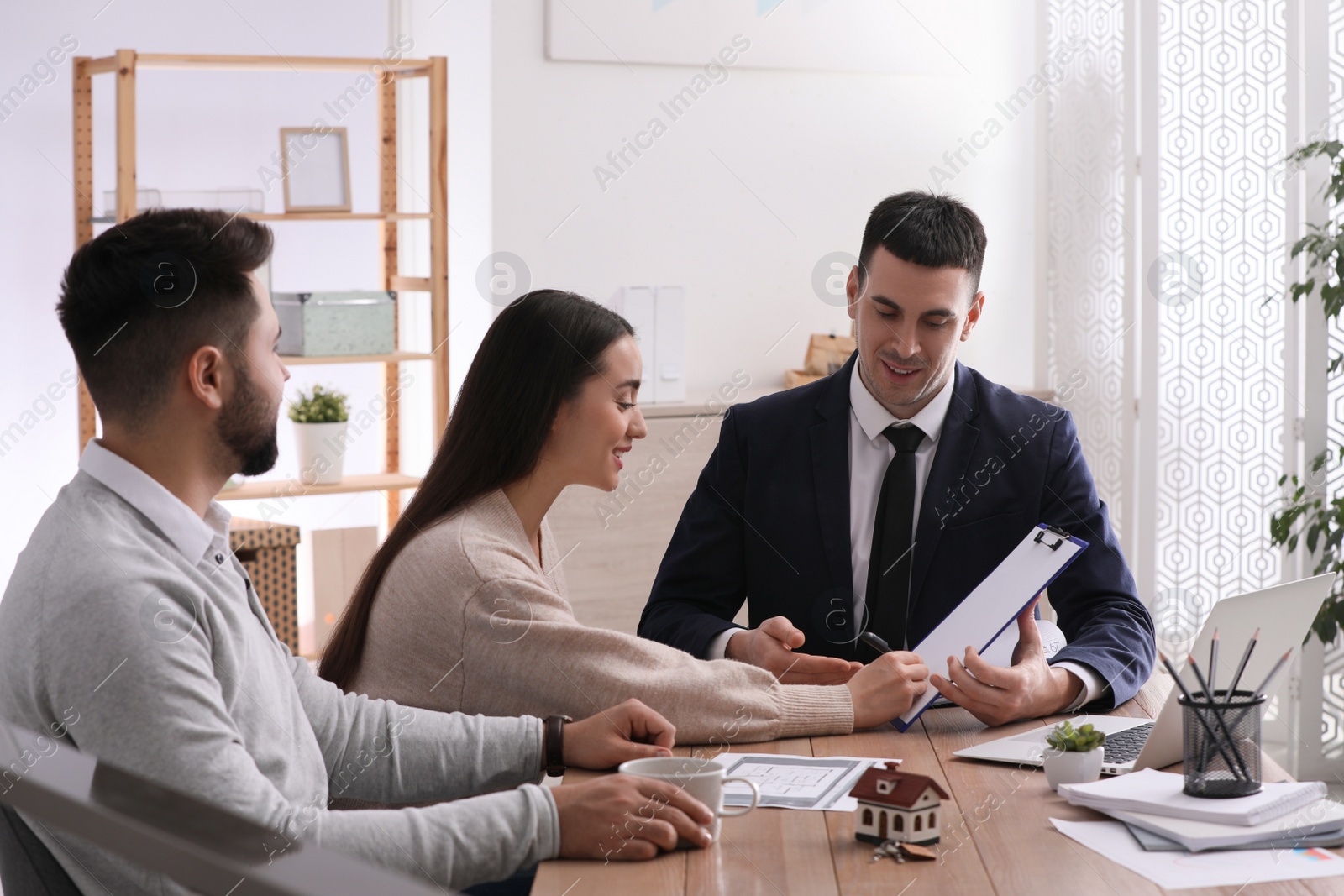 Photo of Happy young couple signing purchase contract in real estate agent's office. Mortgage concept