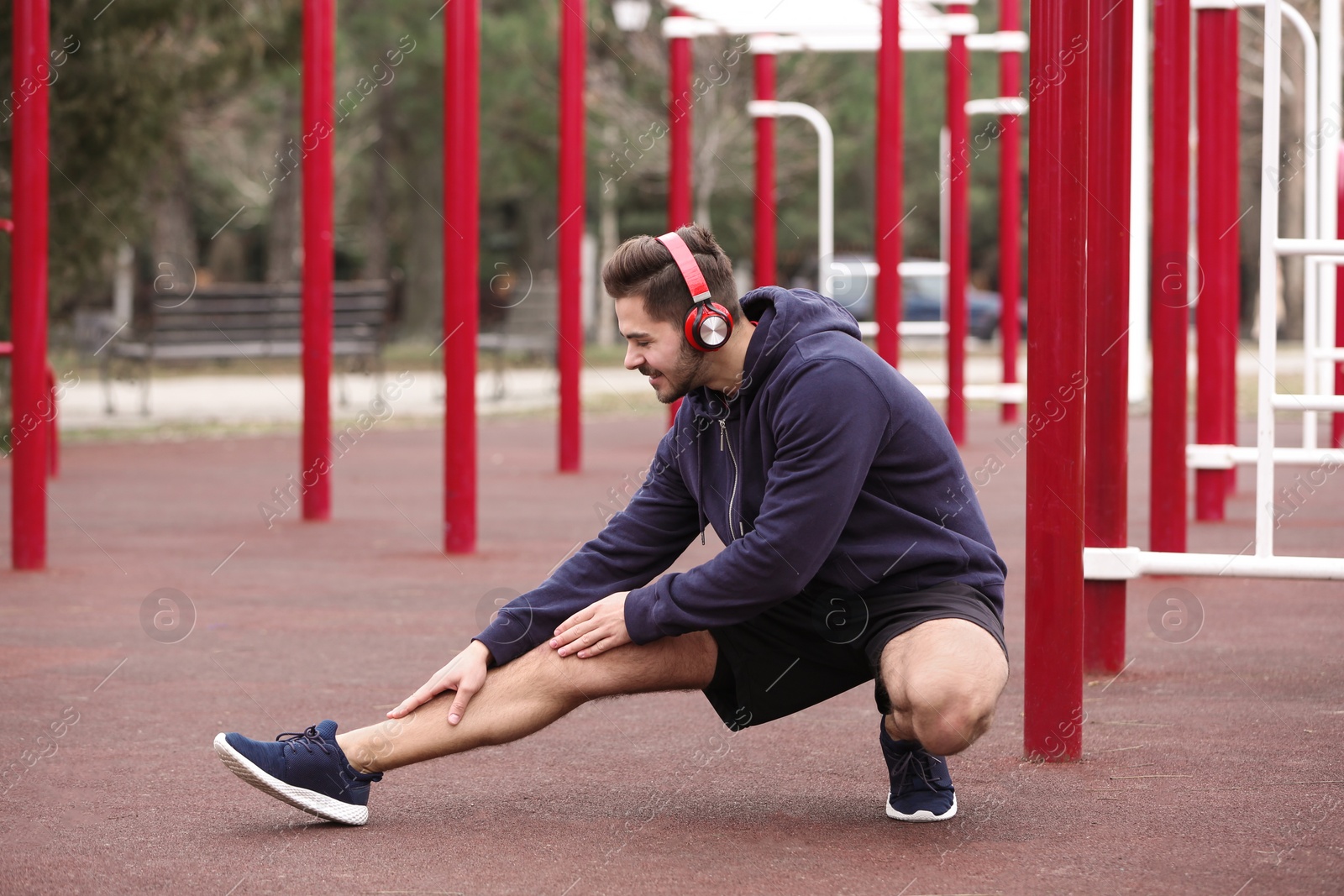 Photo of Young man with headphones listening to music and exercising on sports ground