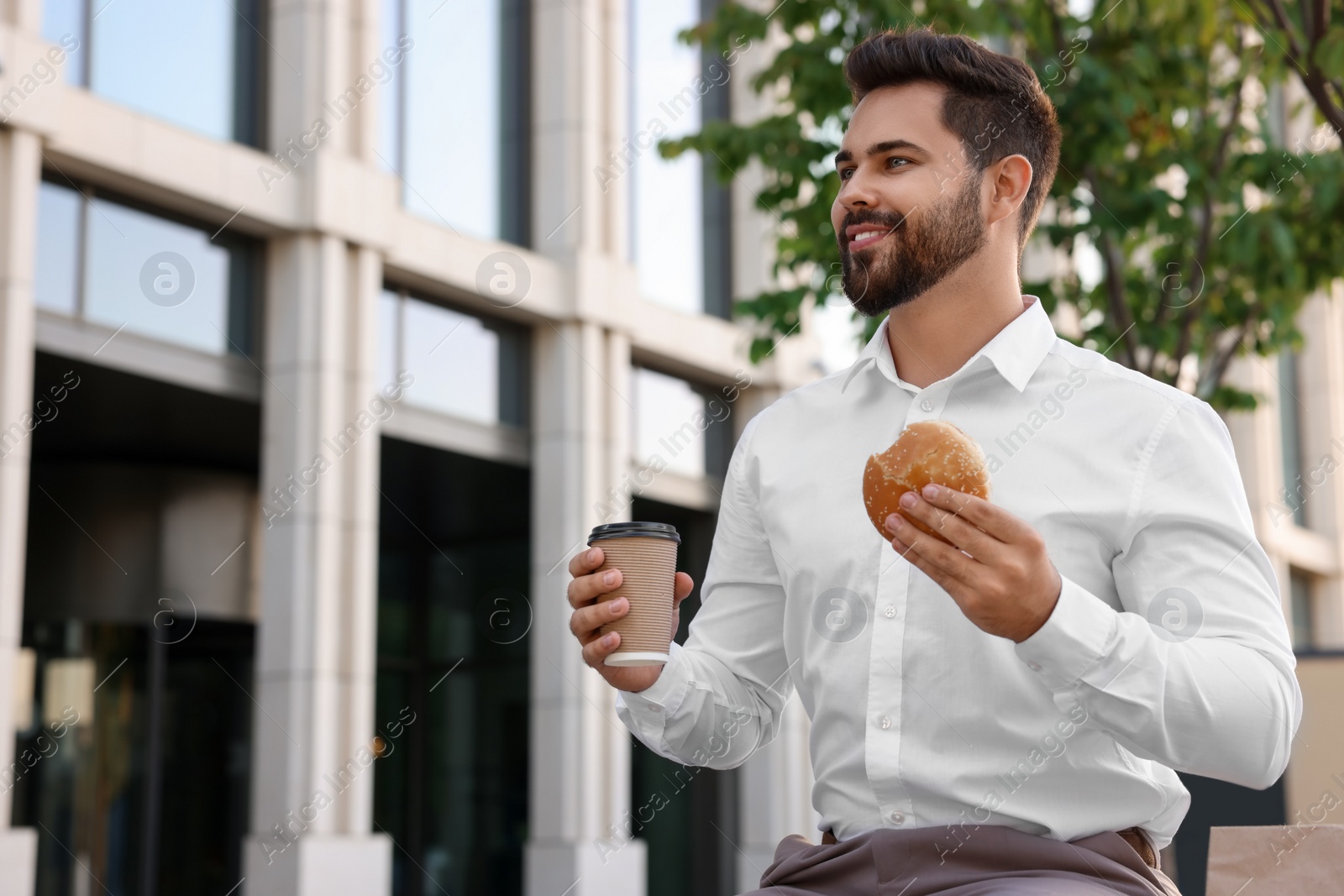 Photo of Businessman with hamburger and paper cup of coffee having lunch outdoors, low angle view