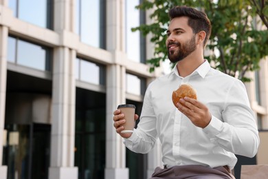 Businessman with hamburger and paper cup of coffee having lunch outdoors, low angle view