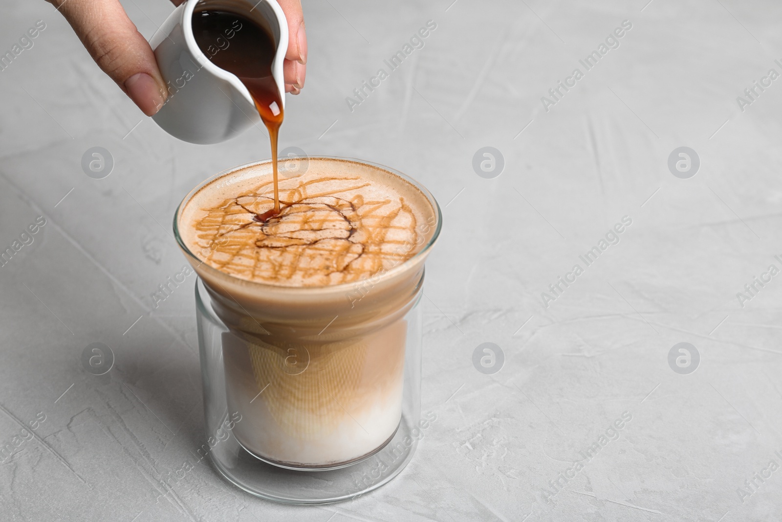 Photo of Woman adding caramel syrup to latte macchiato on table, space for text