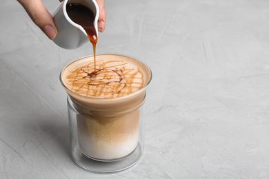 Photo of Woman adding caramel syrup to latte macchiato on table, space for text