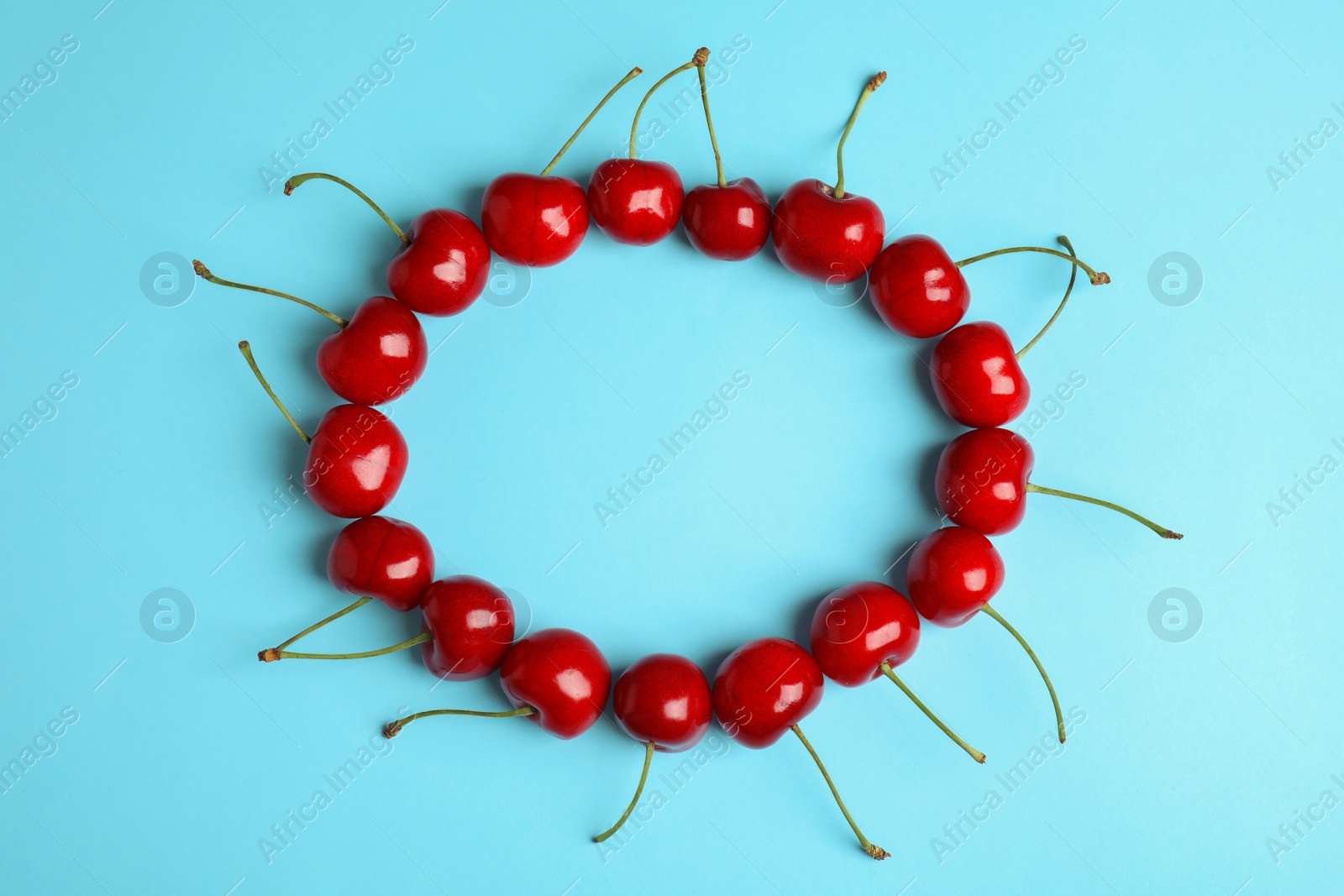 Photo of Frame made of sweet cherries on light blue background, top view. Space for text