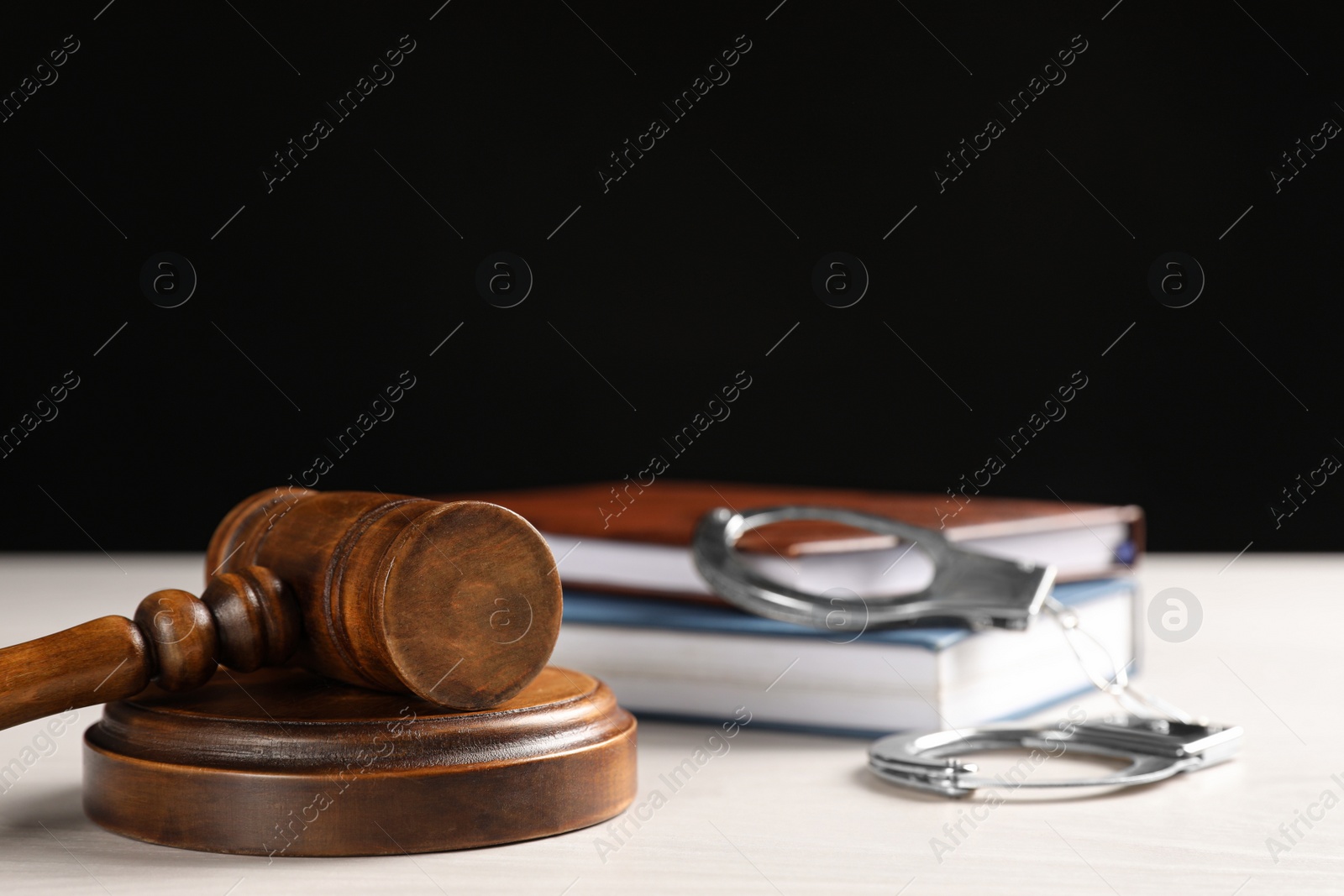 Photo of Judge's gavel, handcuffs and books on white table against black background. Criminal law concept