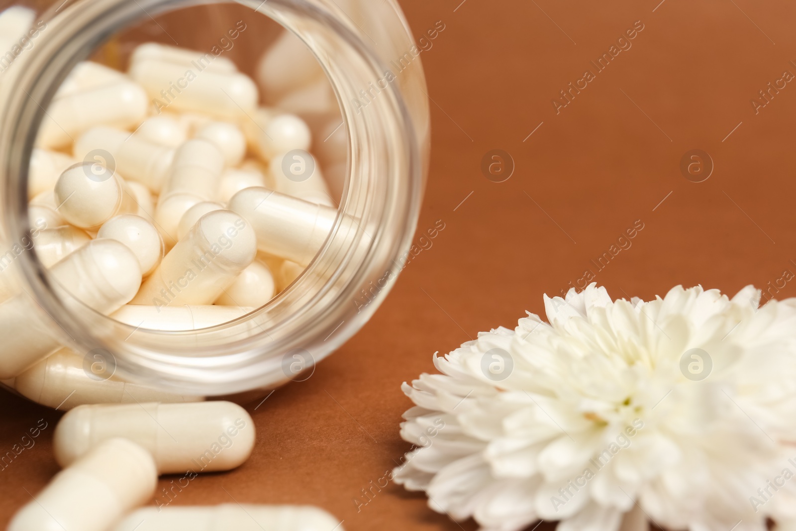 Photo of Open medicine bottle with pills and flower on brown background, closeup
