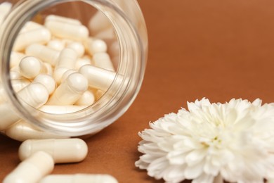 Open medicine bottle with pills and flower on brown background, closeup