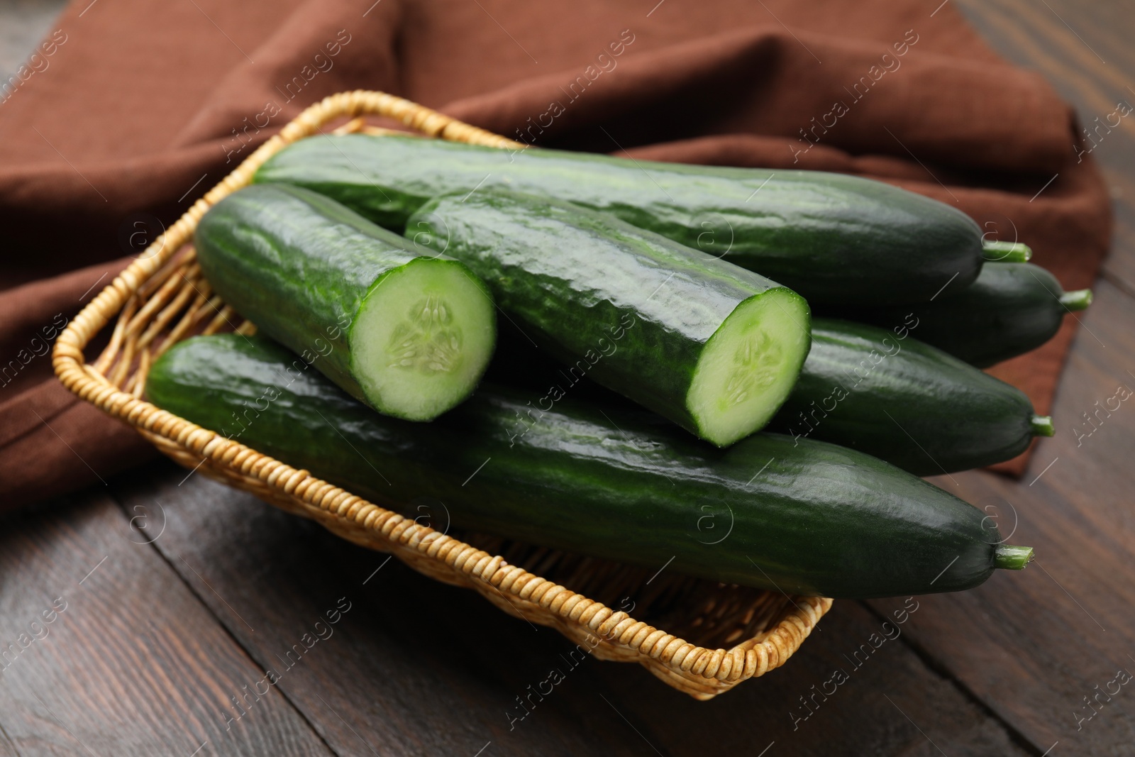 Photo of Fresh cucumbers in wicker basket on wooden table, closeup