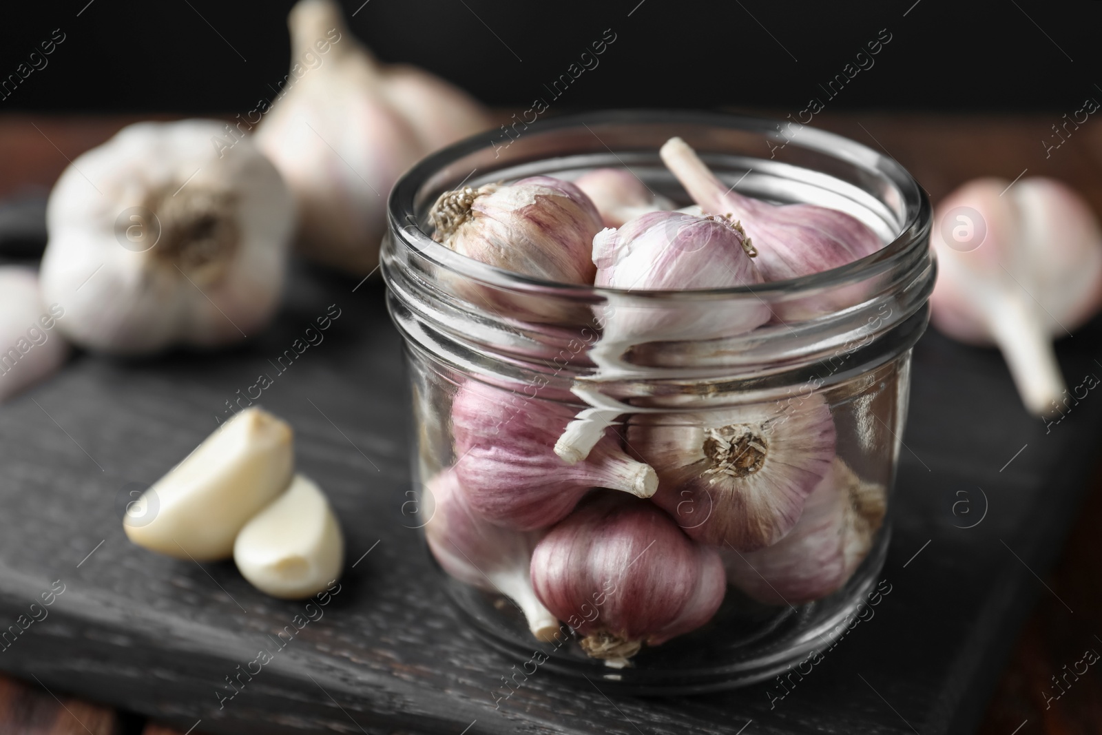 Photo of Many fresh garlic bulbs in jar on black board, closeup. Space for text