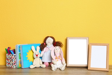Photo of Soft toys and photo frames on table against yellow background, space for text. Child room interior