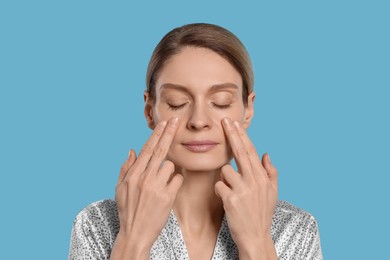 Photo of Woman massaging her face on turquoise background