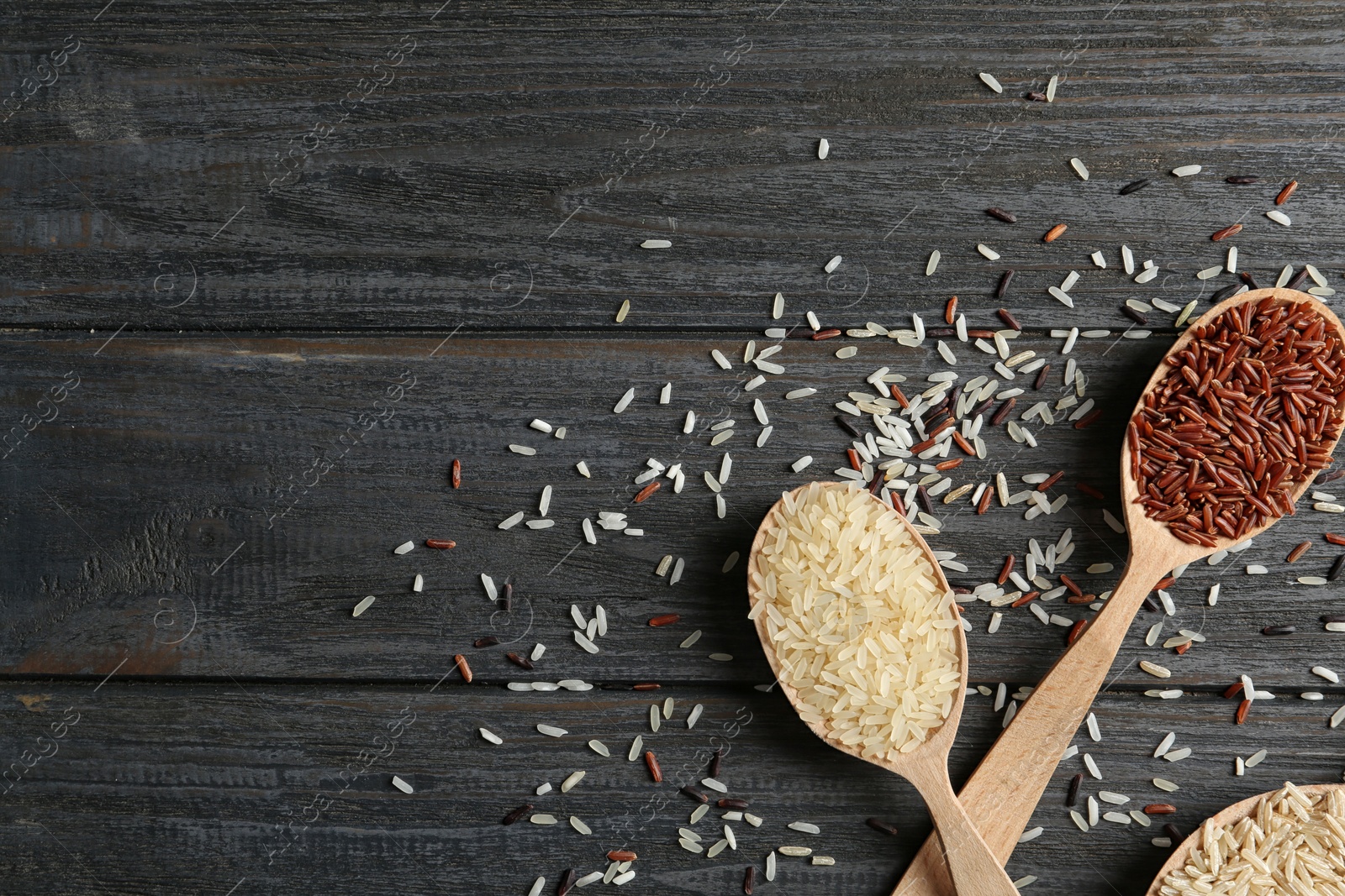 Photo of Flat lay composition with brown and other types of rice in spoons on wooden background. Space for text