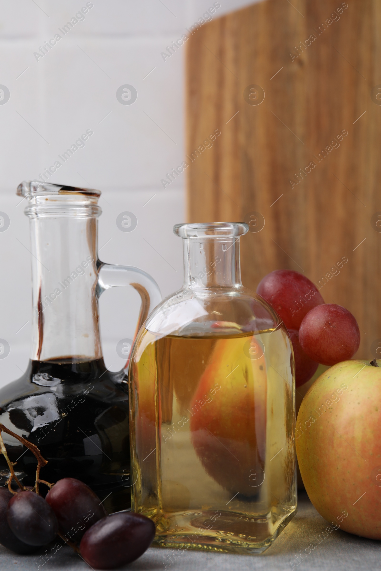 Photo of Different types of vinegar and fresh fruits on grey table