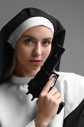 Woman in nun habit holding handgun on grey background, closeup