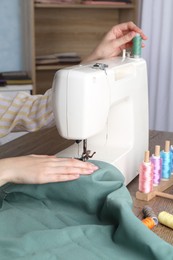 Photo of Seamstress working with sewing machine at wooden table indoors, closeup