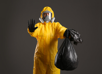 Photo of Woman in chemical protective suit holding trash bag on grey background. Virus research