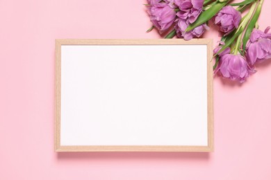 Empty photo frame and beautiful flowers on pink background, flat lay. Space for design