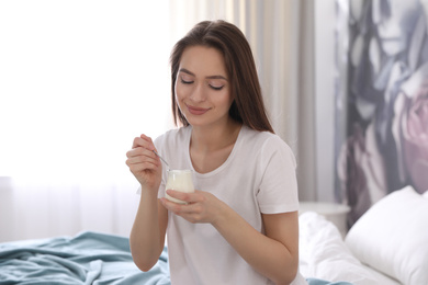Photo of Young attractive woman with tasty yogurt on bed at home