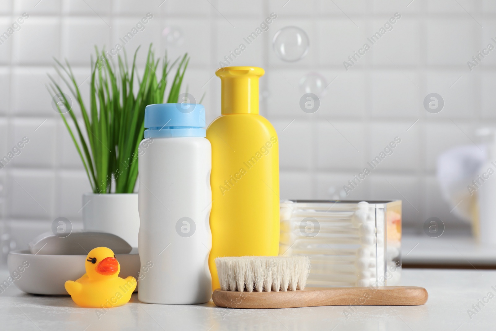 Photo of Baby cosmetic products, bath duck, brush and cotton swabs on white against soap bubbles