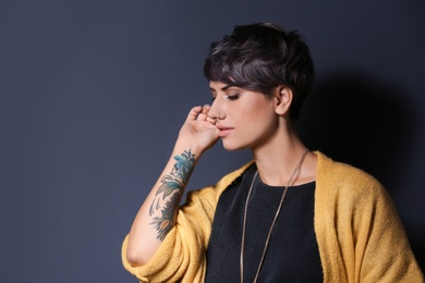 Trendy young woman with tattoo on grey background. Space for text