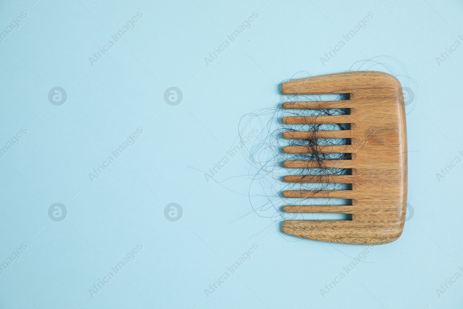 Photo of Wooden comb with lost hair on light blue background, top view. Space for text