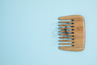 Photo of Wooden comb with lost hair on light blue background, top view. Space for text