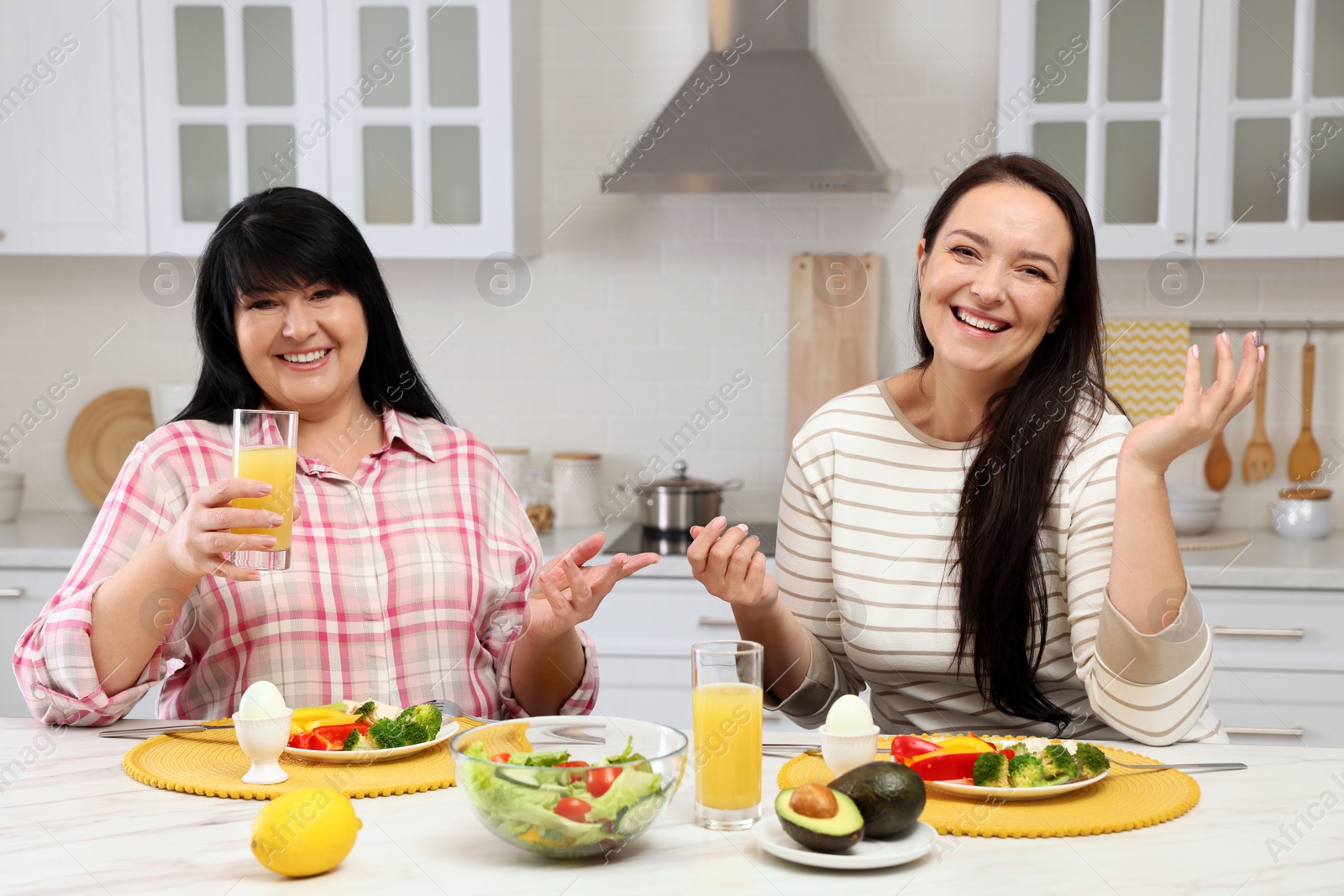 Photo of Happy overweight women having healthy meal together at table in kitchen