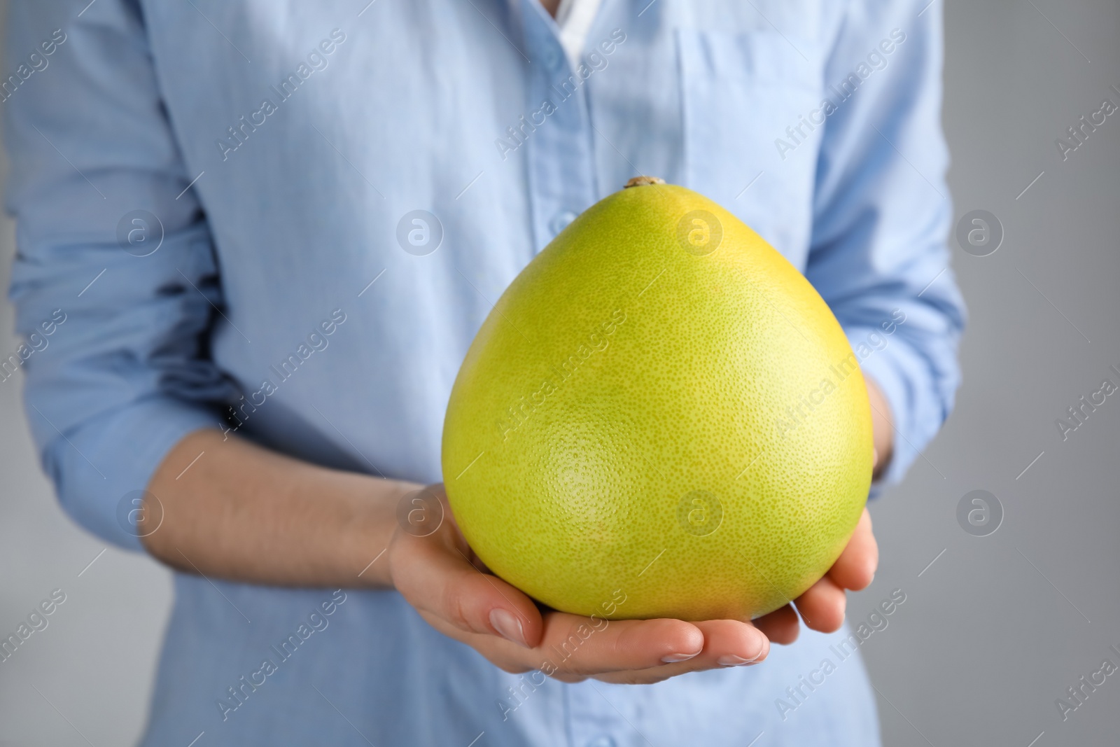 Photo of Woman holding fresh whole pomelo on light grey background, closeup