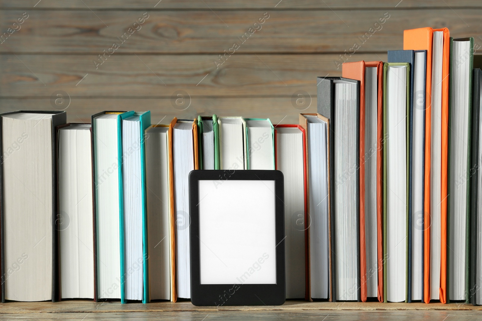 Photo of Portable e-book reader and many hardcover books on wooden table