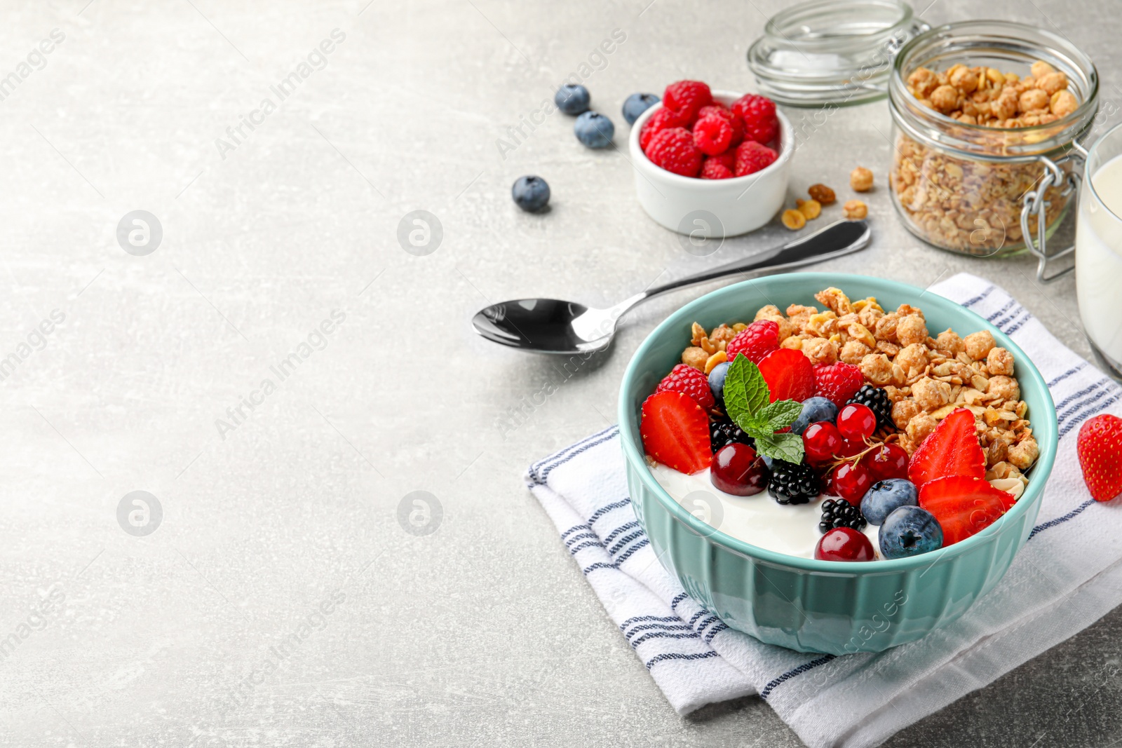 Photo of Bowl with tasty granola and berries on light grey table. Space for text