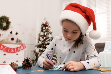 Cute little child making Christmas craft at blue wooden table in decorated room