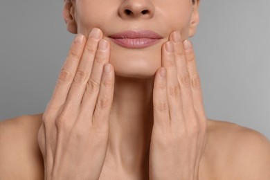 Woman massaging her face on grey background, closeup