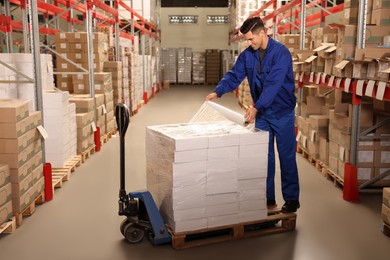 Worker wrapping boxes in stretch film at warehouse