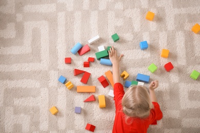 Photo of Cute little girl lying on cozy carpet with cubes at home