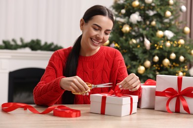 Happy woman decorating Christmas gift box at wooden table in room