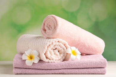 Photo of Soft folded towels and plumeria flowers on white wooden table