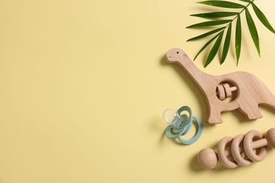 Photo of Baby accessory. Wooden rattles, pacifier and palm leaf on yellow background, flat lay. Space for text