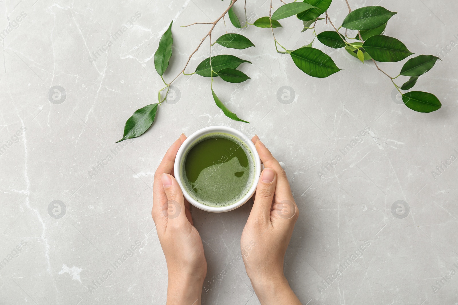 Photo of Woman with cup of matcha tea and leaves at table, top view