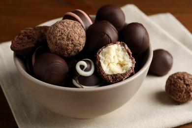 Photo of Bowl with many different delicious chocolate truffles on wooden table