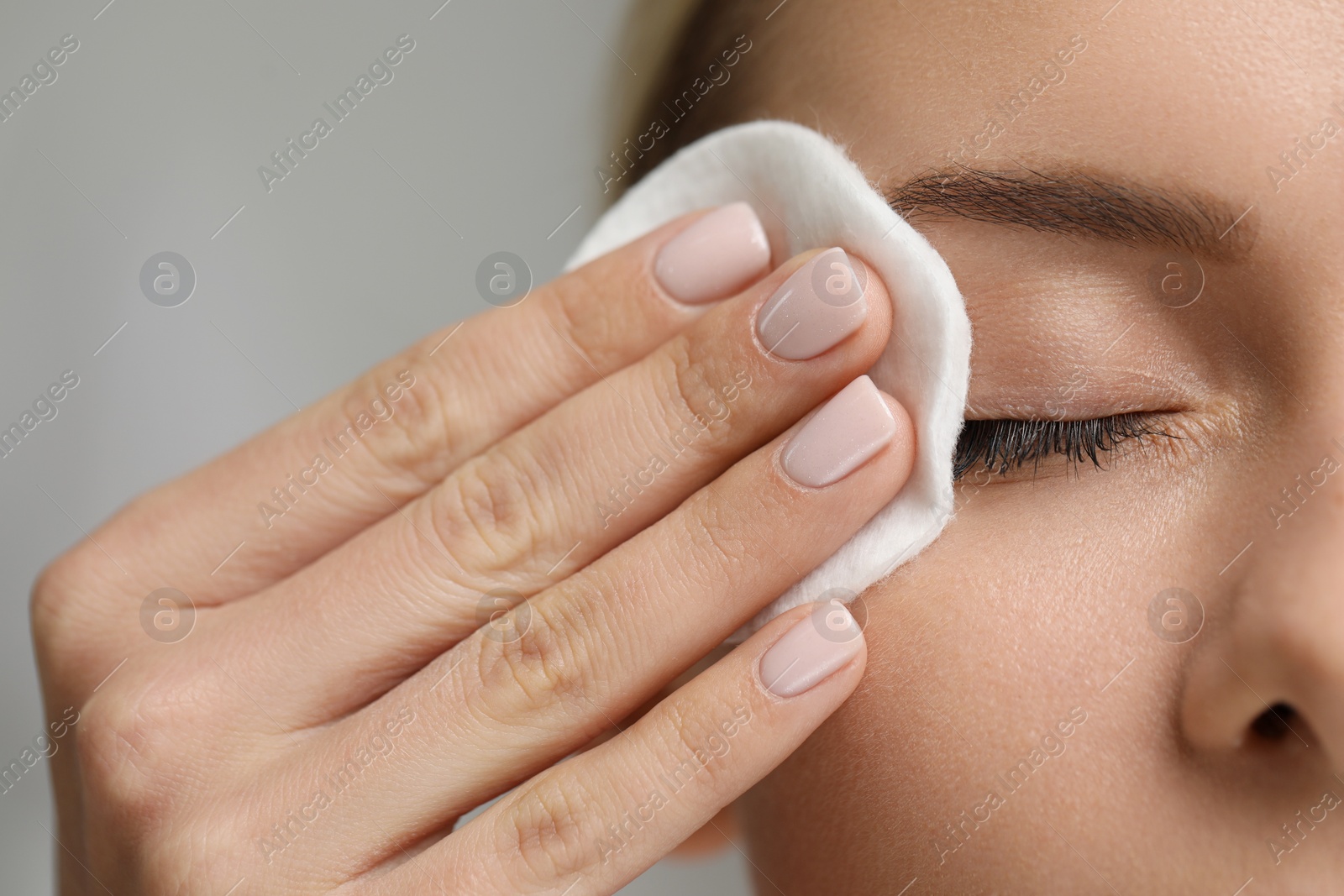 Photo of Woman removing makeup with cotton pad on grey background, closeup