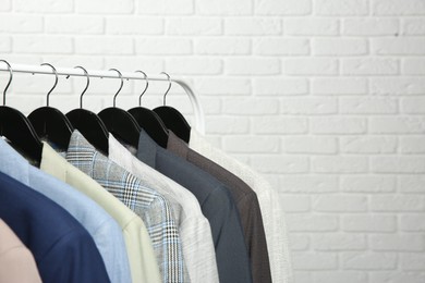 Dry-cleaning service. Many different clothes hanging on rack against white brick wall, space for text