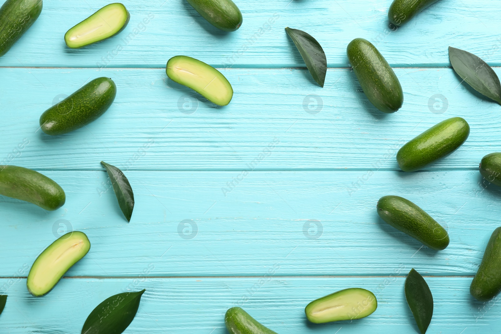 Photo of Frame made of fresh seedless avocados with green leaves on turquoise wooden table, flat lay. Space for text