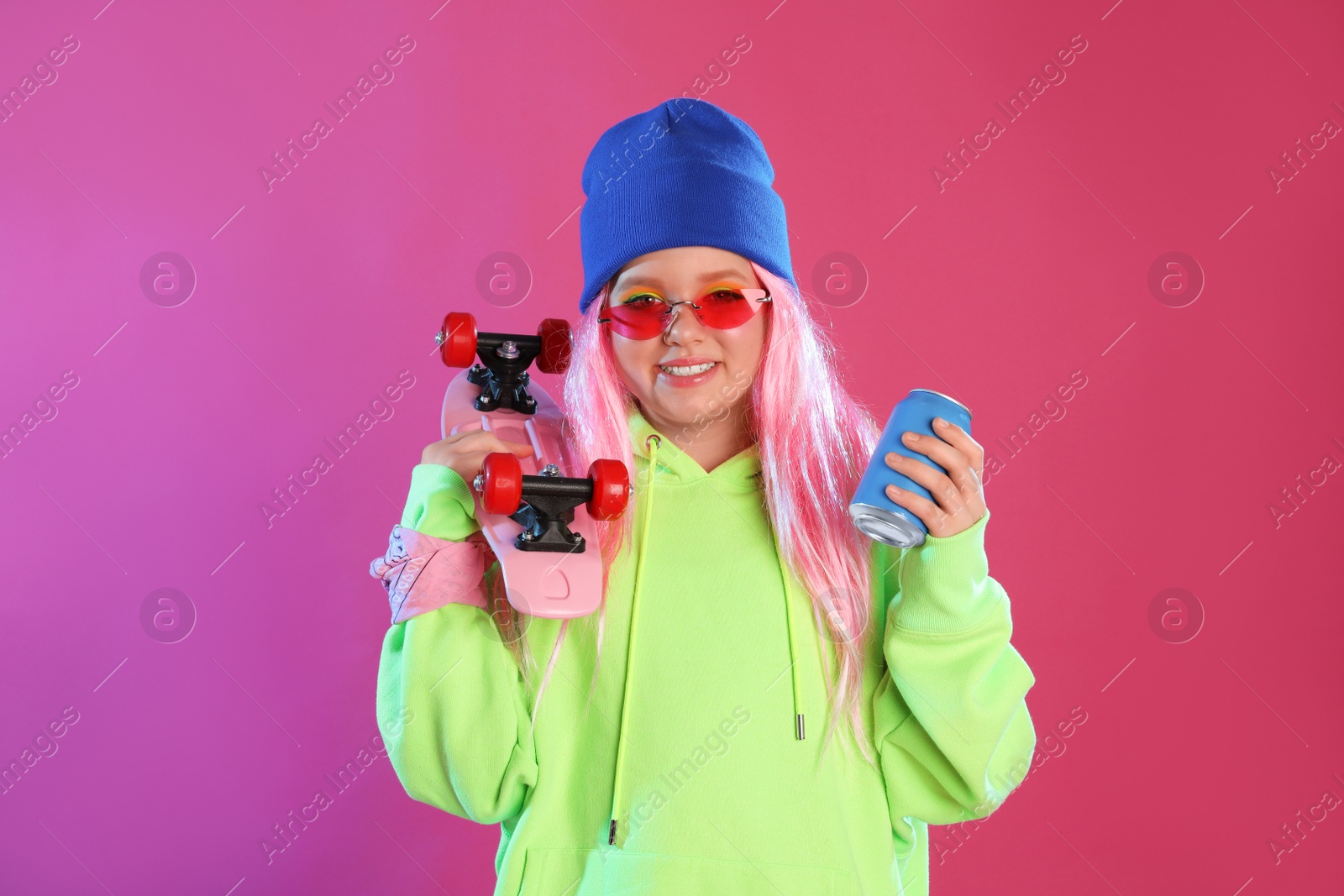 Photo of Cute indie girl with canned drink and penny board on violet background