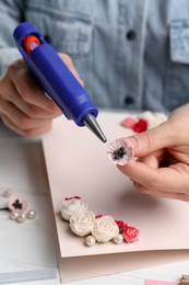 Woman using hot glue gun to make craft at white table, closeup