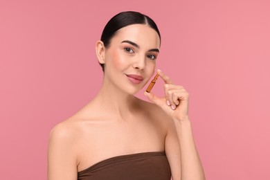 Beautiful young woman holding skincare ampoule on pink background