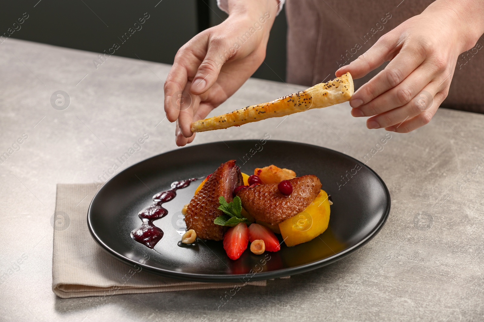 Photo of Food stylist preparing delicious dish with chicken, parsnip and strawberries for photoshoot at grey table in studio, closeup