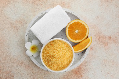 Photo of Sea salt, towel, plumeria flower and cut orange on beige textured table, top view